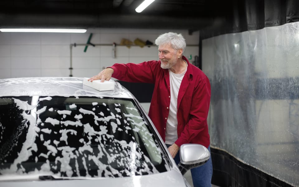 Hombre lavando su coche en casa, con productos de calidad y herramientas necesarias
