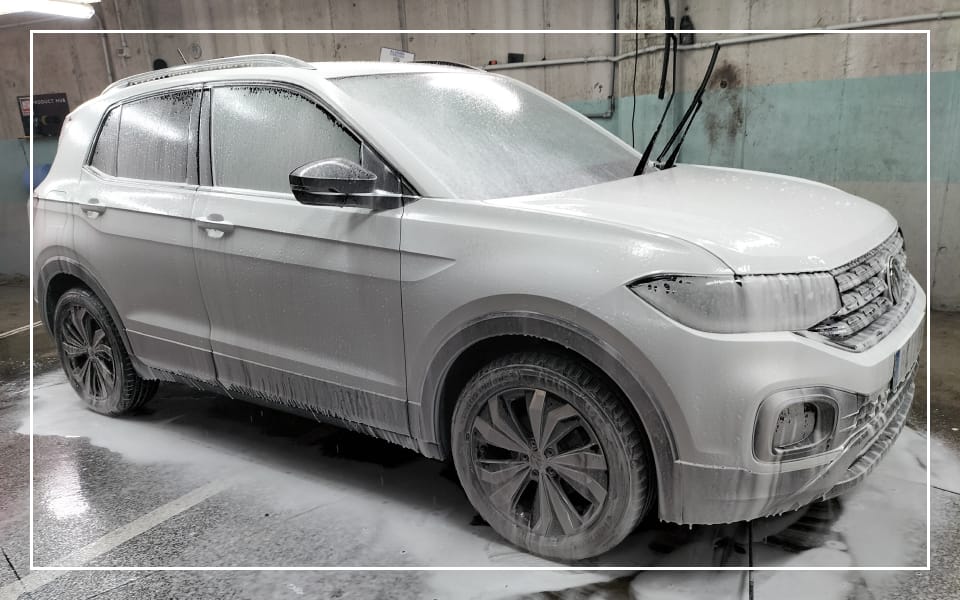 Coche SUV cubierto de espuma activa durante un proceso de lavado exterior premium