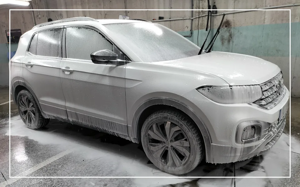 Coche SUV cubierto de espuma activa durante un proceso de lavado exterior premium