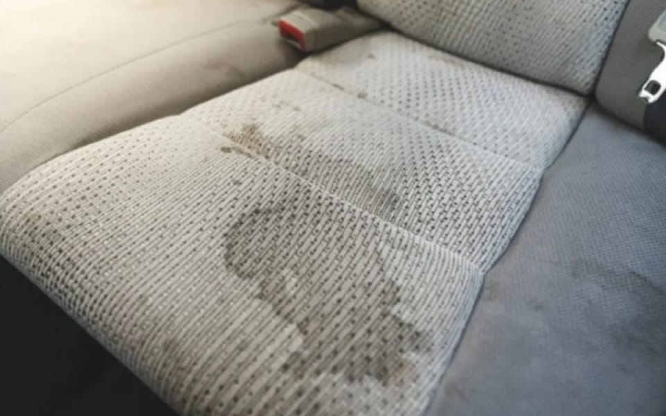 Asiento trasero de tela con manchas de líquidos y suciedad incrustada